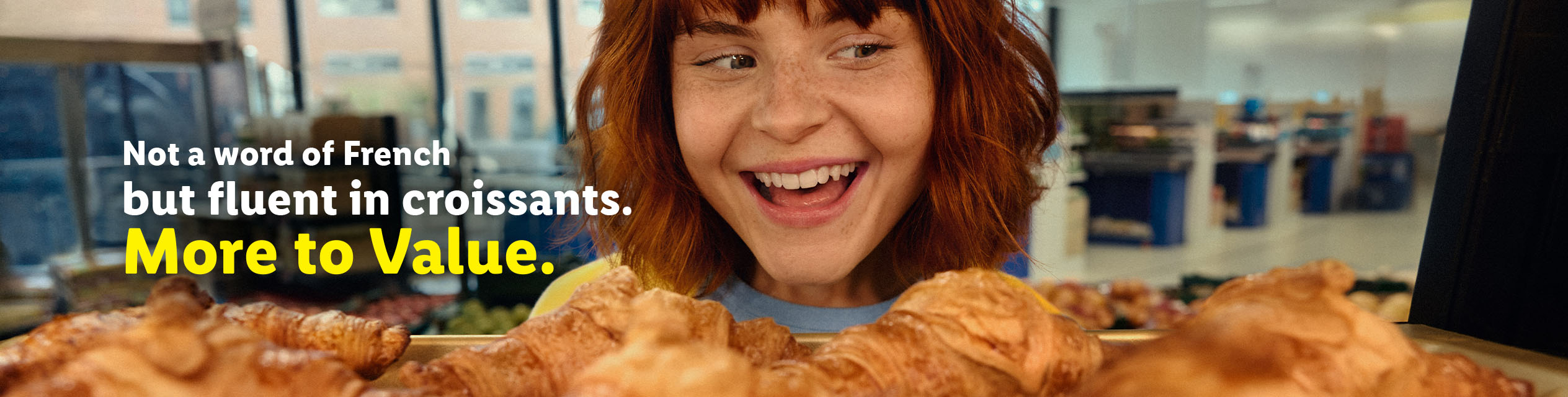 A smiling woman with red hair looks at a tray of croissants, with text about being fluent in croissants.