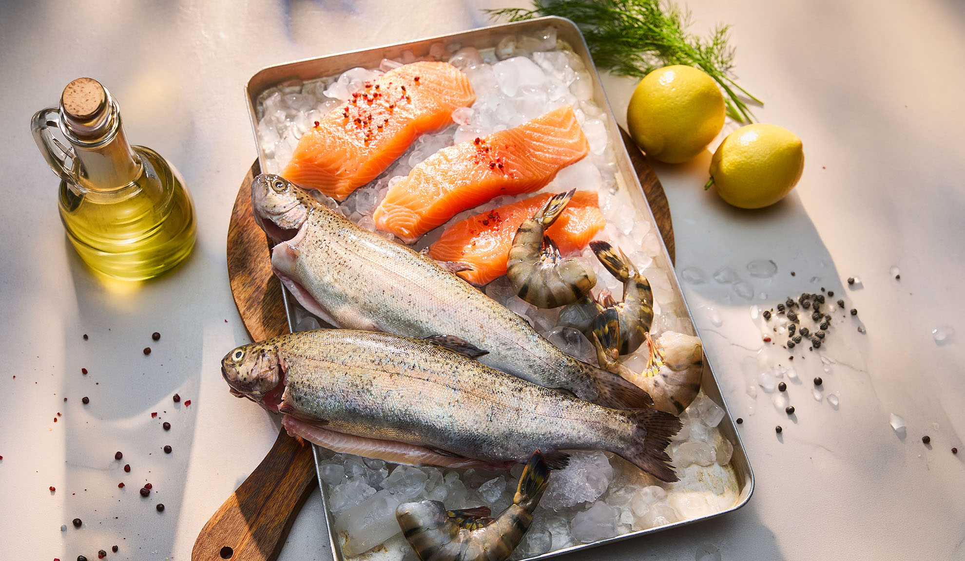 Fresh fish, salmon fillets, and shrimp on ice, with lemons and oil.