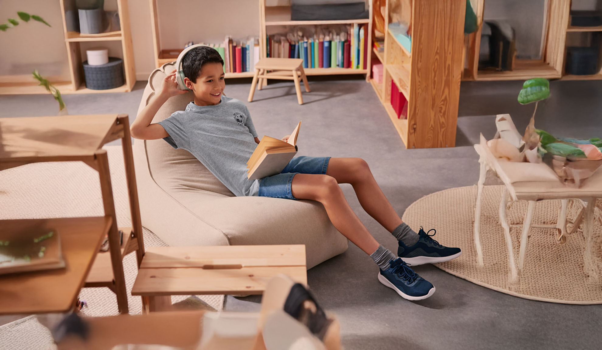 A boy relaxes in a beanbag chair, wearing headphones and reading a book.