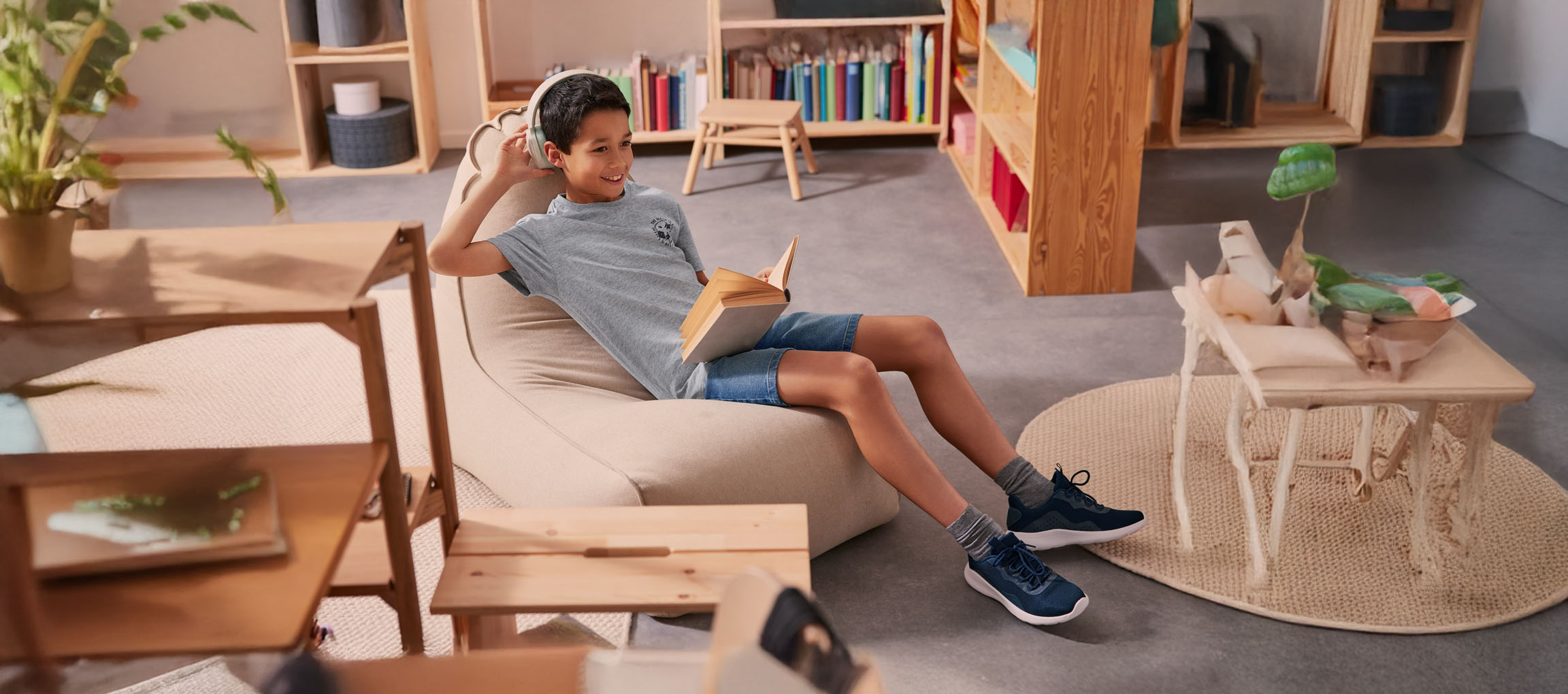 Boy relaxes in a beanbag chair, reading a book while wearing headphones.