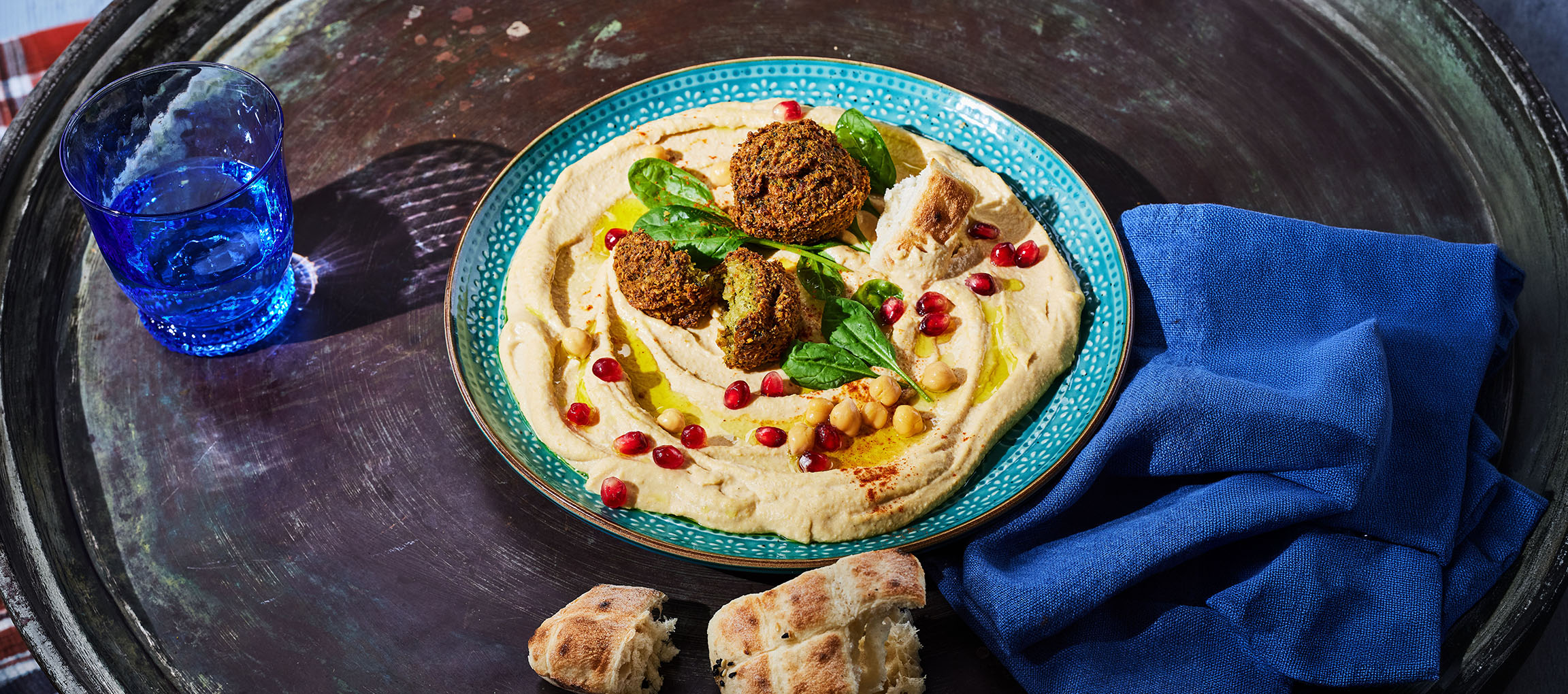 Hummus with falafel, pomegranate seeds, and bread on a metal tray.