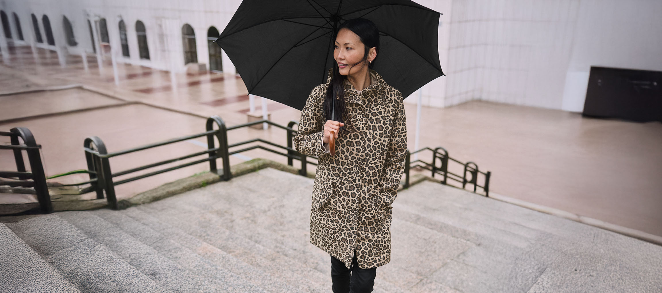 Woman in leopard print coat with umbrella on stairs.