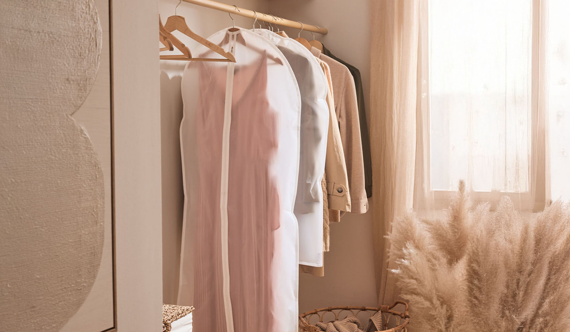 Clothing in transparent garment bags hangs on a clothes rail in a bright room.