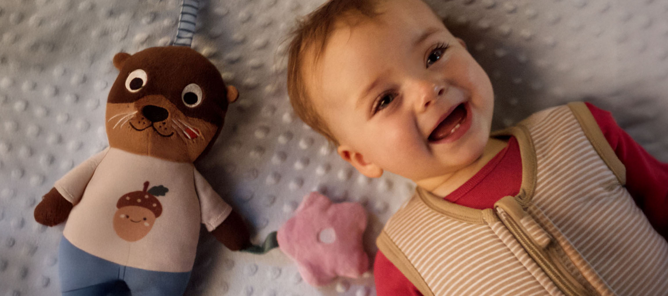 Smiling baby and a plush toy with an acorn on its belly.