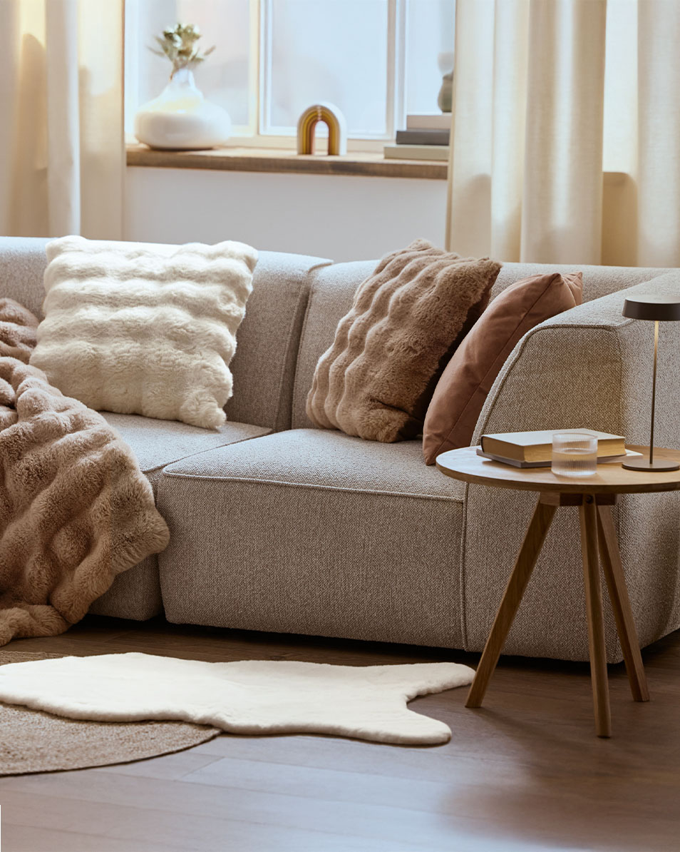 Gray modular sofa with fluffy pillows and throws, wooden side table.