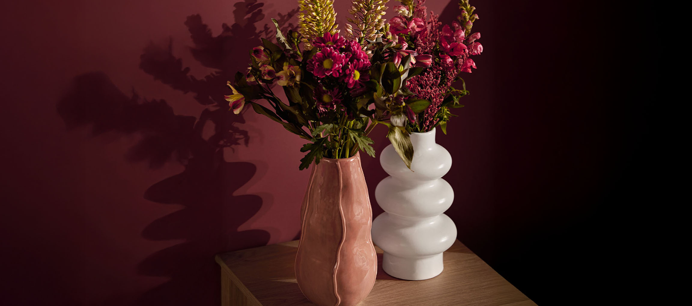 Two vases with flowers, one pink and one white, on a wooden surface.