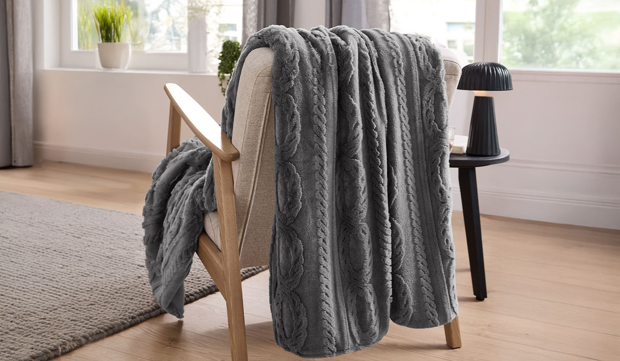 A gray cable-knit throw blanket draped over a light wood armchair in a living room.