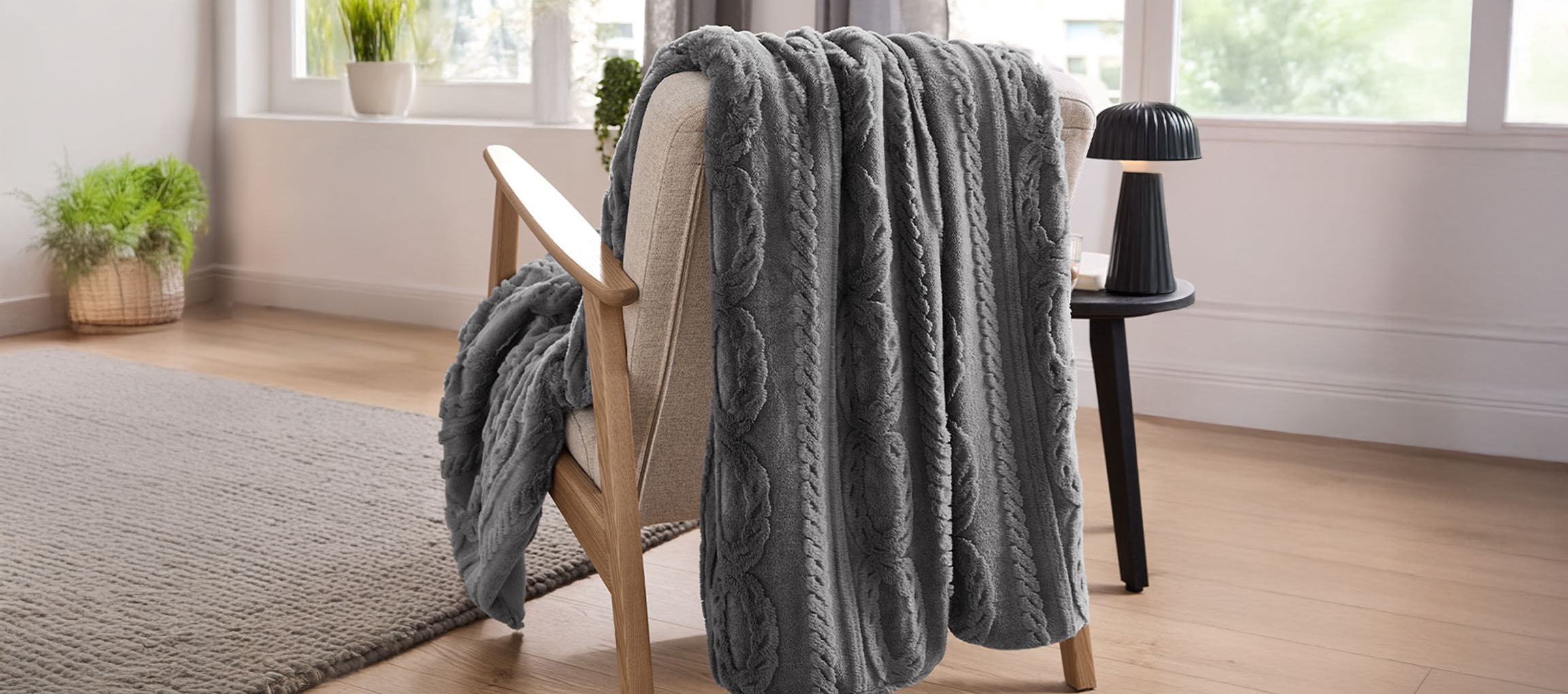 Gray cable knit throw blanket draped over a light wood armchair in a bright room.