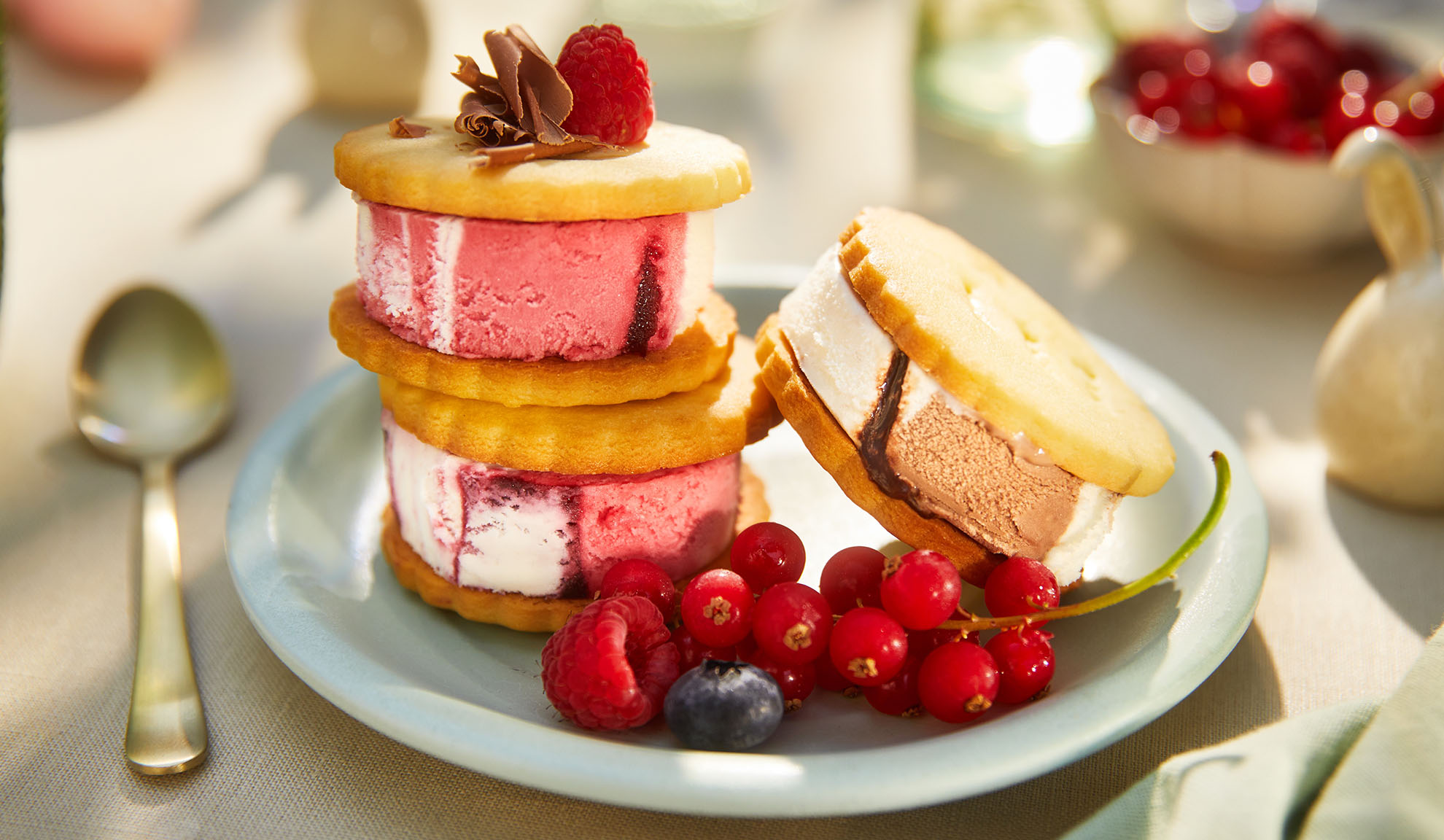 Ice cream sandwiches with berries on a light blue plate in a sunny outdoor setting.