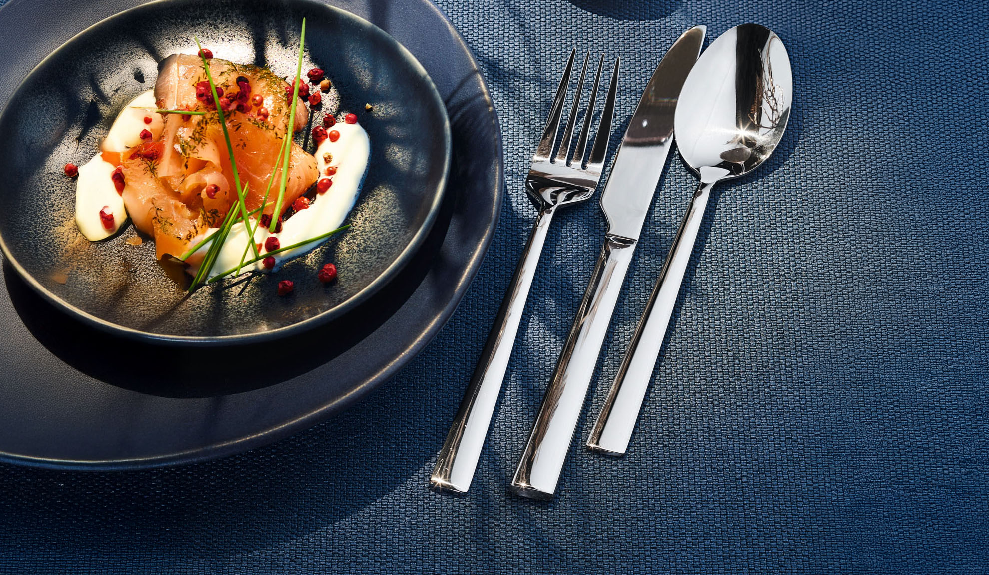 Smoked salmon with cream, herbs, and pink peppercorns on a dark plate with cutlery.