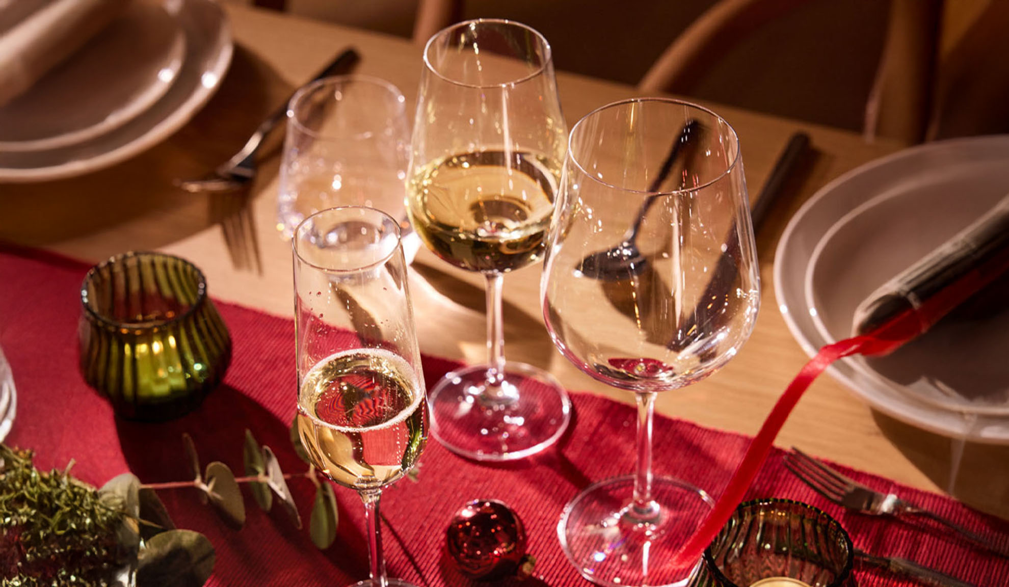 Festive table set with wine glasses, a champagne flute, and Christmas decorations.