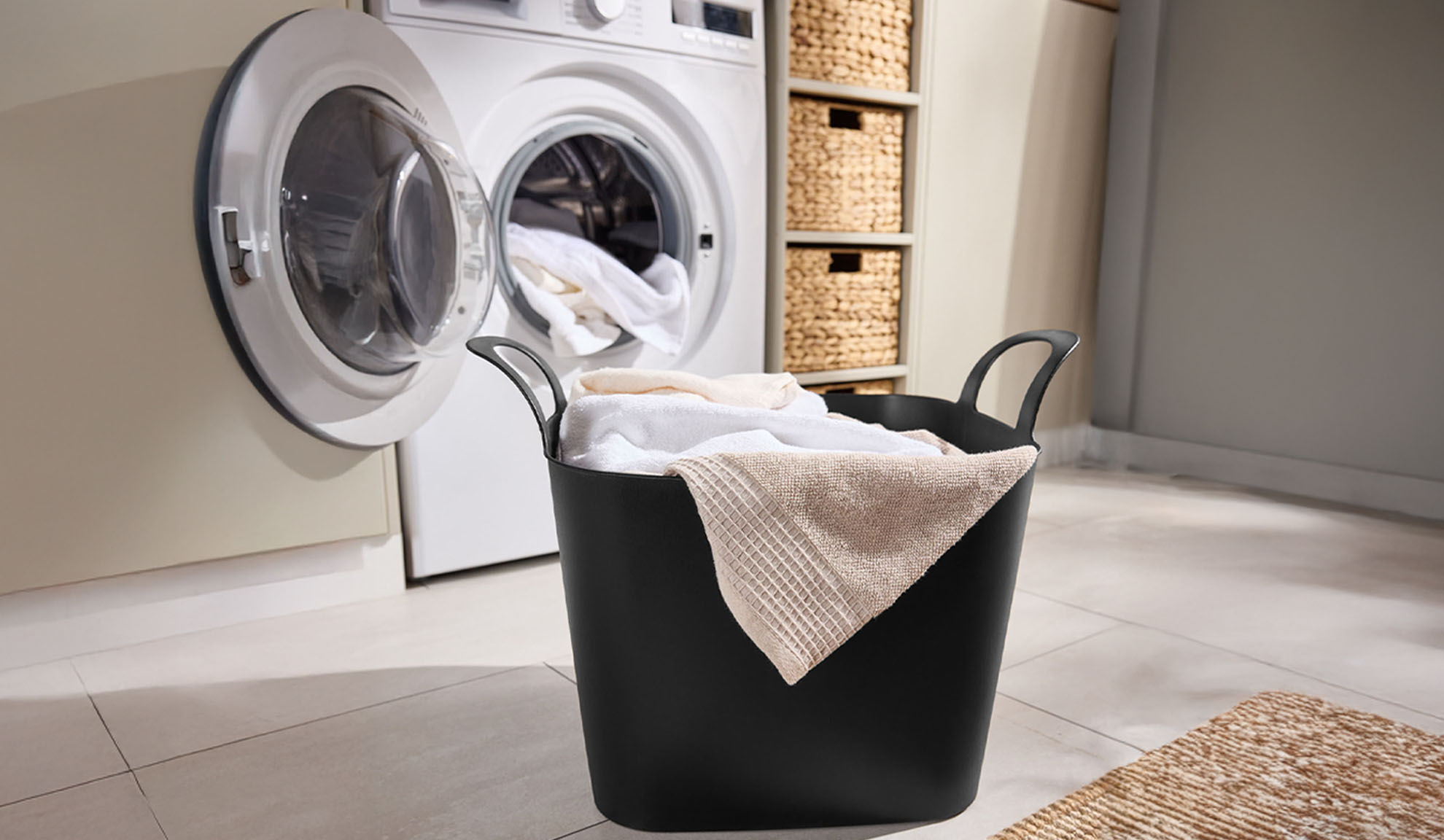 Washing machine with open door and a black laundry basket full of towels