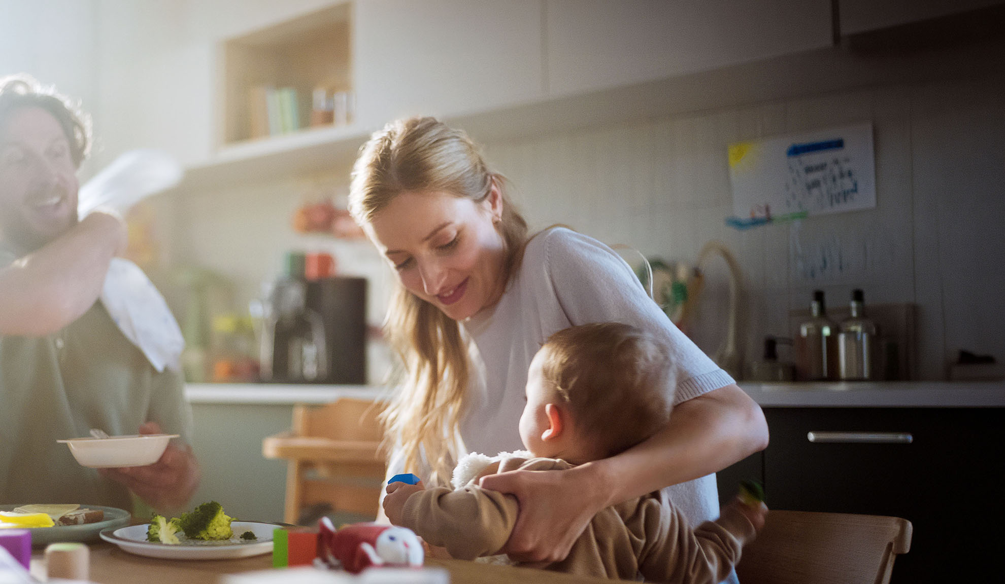 Family eating together in the kitchen, mother helping baby eat.