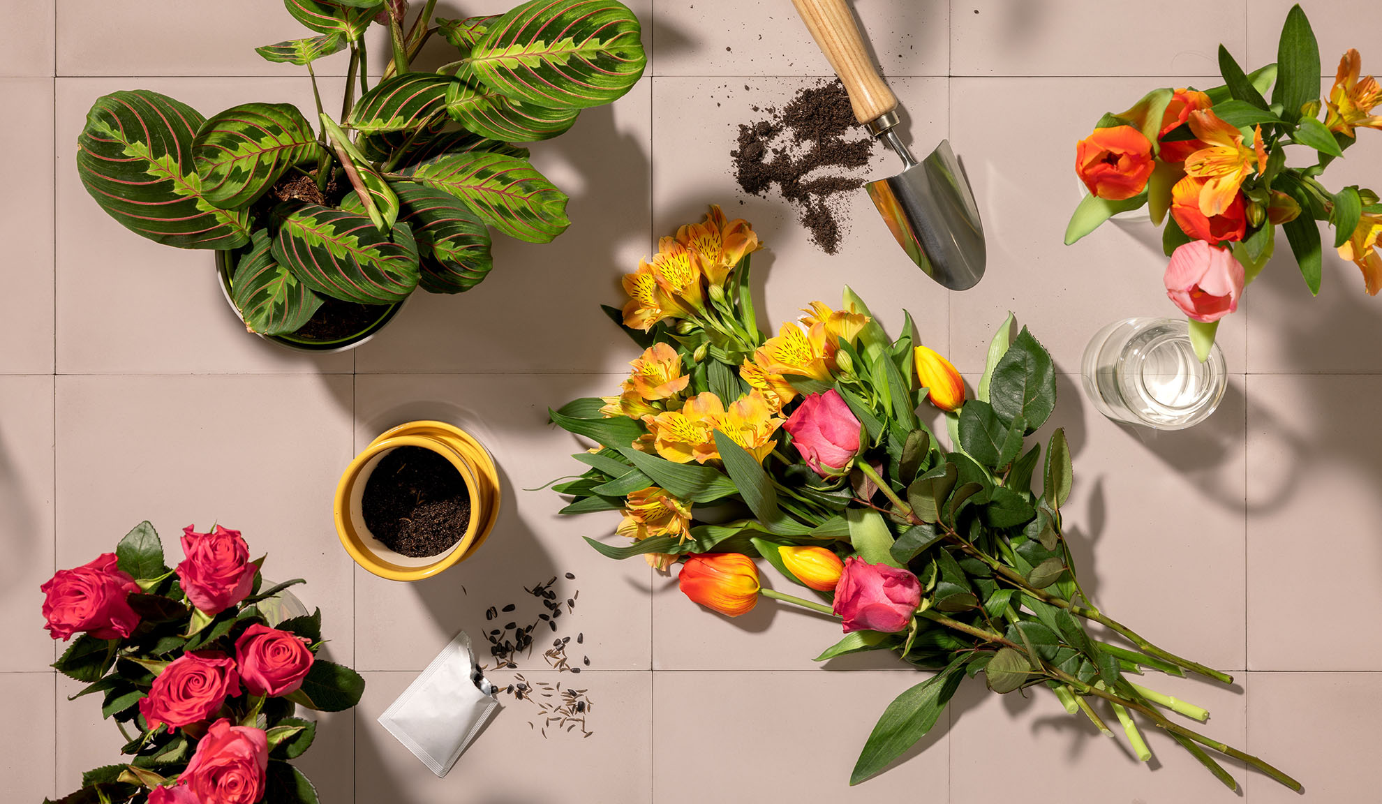 Overhead shot of gardening tools, potted plants, and bouquets of colorful flowers on a tiled surface.