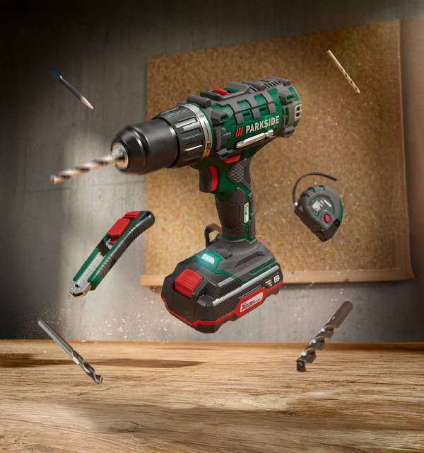 Cordless drill with battery, utility knife, tape measure, and drill bits in mid-air.