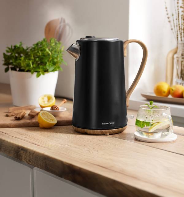 Black kettle with wooden accents on a kitchen counter with lemons and herbs.