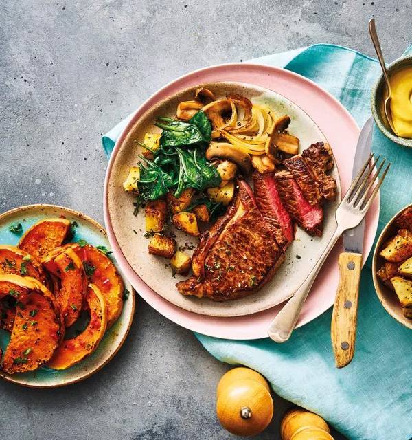 Steak with roasted potatoes, spinach, mushrooms, and butternut squash on a rustic plate.