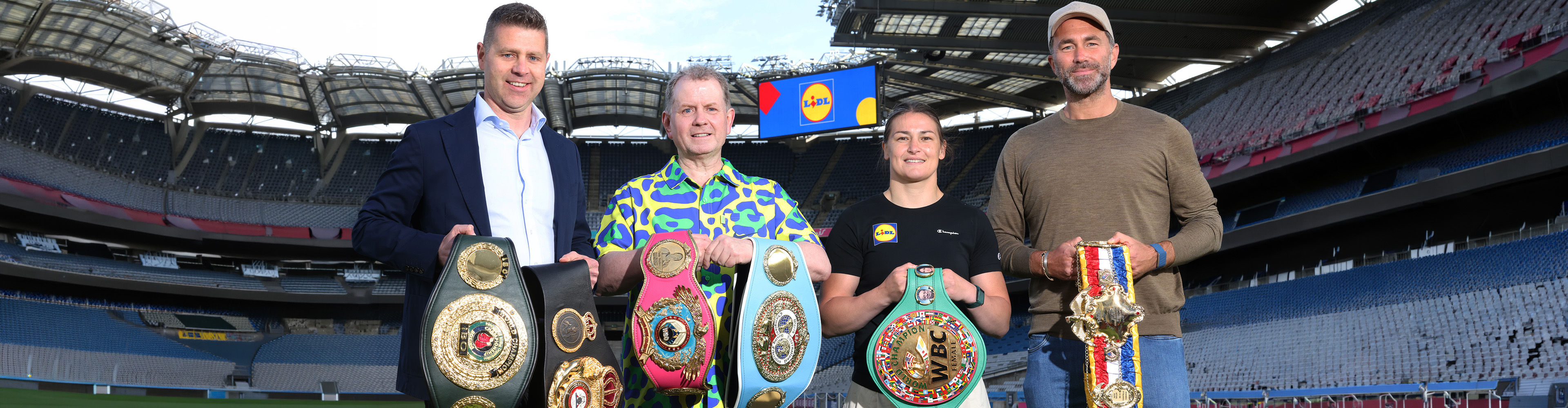 Four people, including a female boxer, holding championship belts in a stadium.