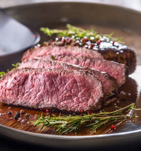 Sliced steak with herbs and spices on a wooden board.