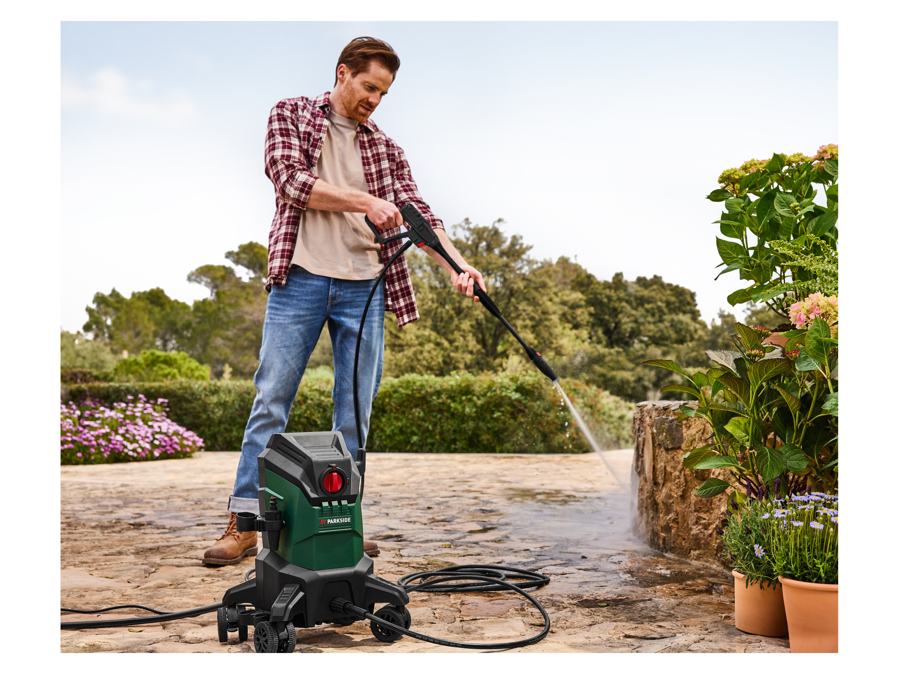 A man uses a Parkside pressure washer to clean a stone patio.