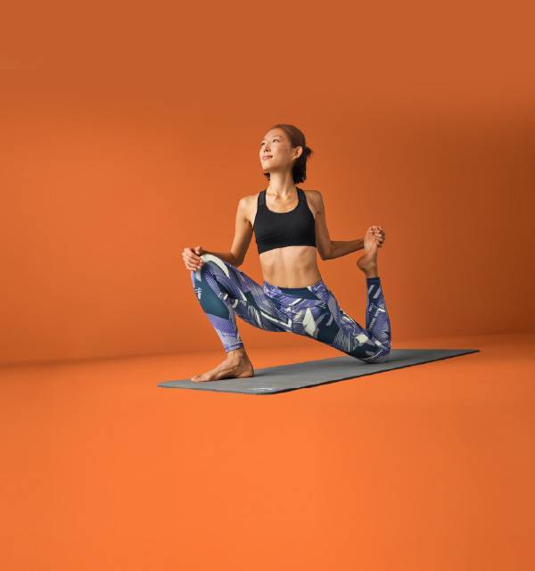 Woman in a black sports bra and patterned leggings doing a yoga pose on a mat.