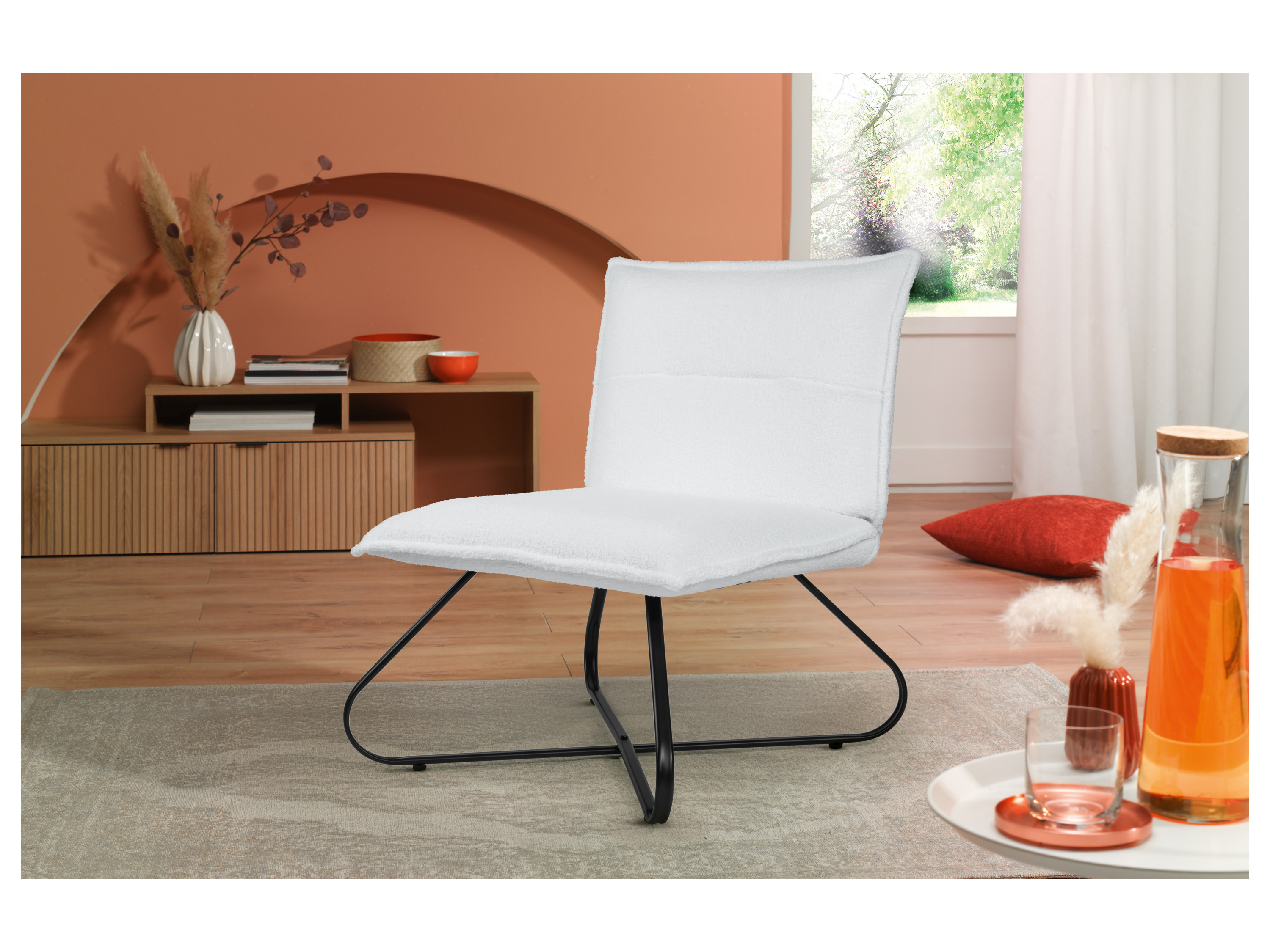 A white upholstered chair with black metal legs on a rug in a living room.