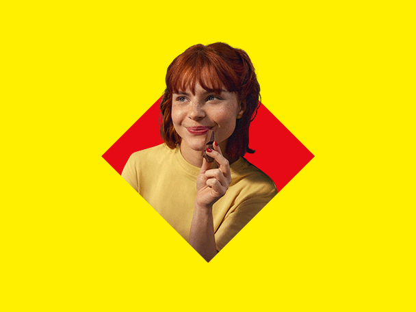 A smiling red-haired woman holding a chocolate against a yellow and red background.
