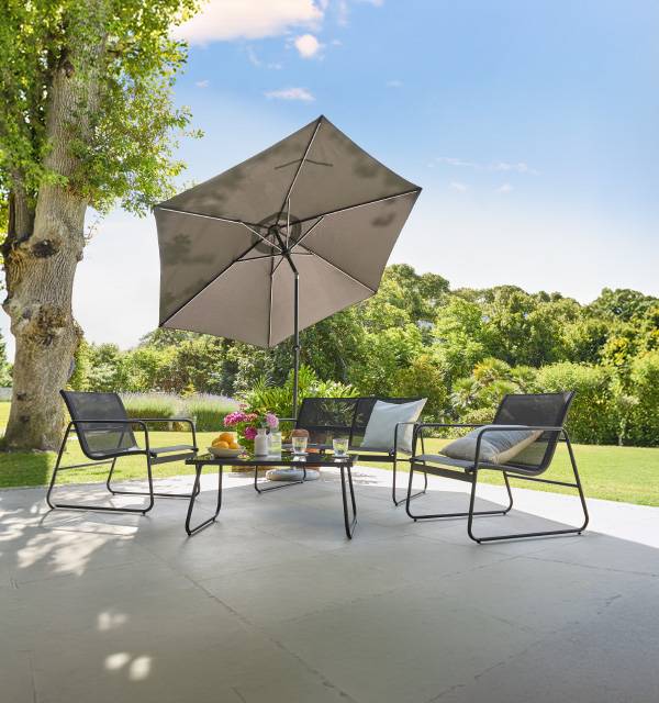 Outdoor patio furniture set with a table, chairs, and a parasol under a tree.