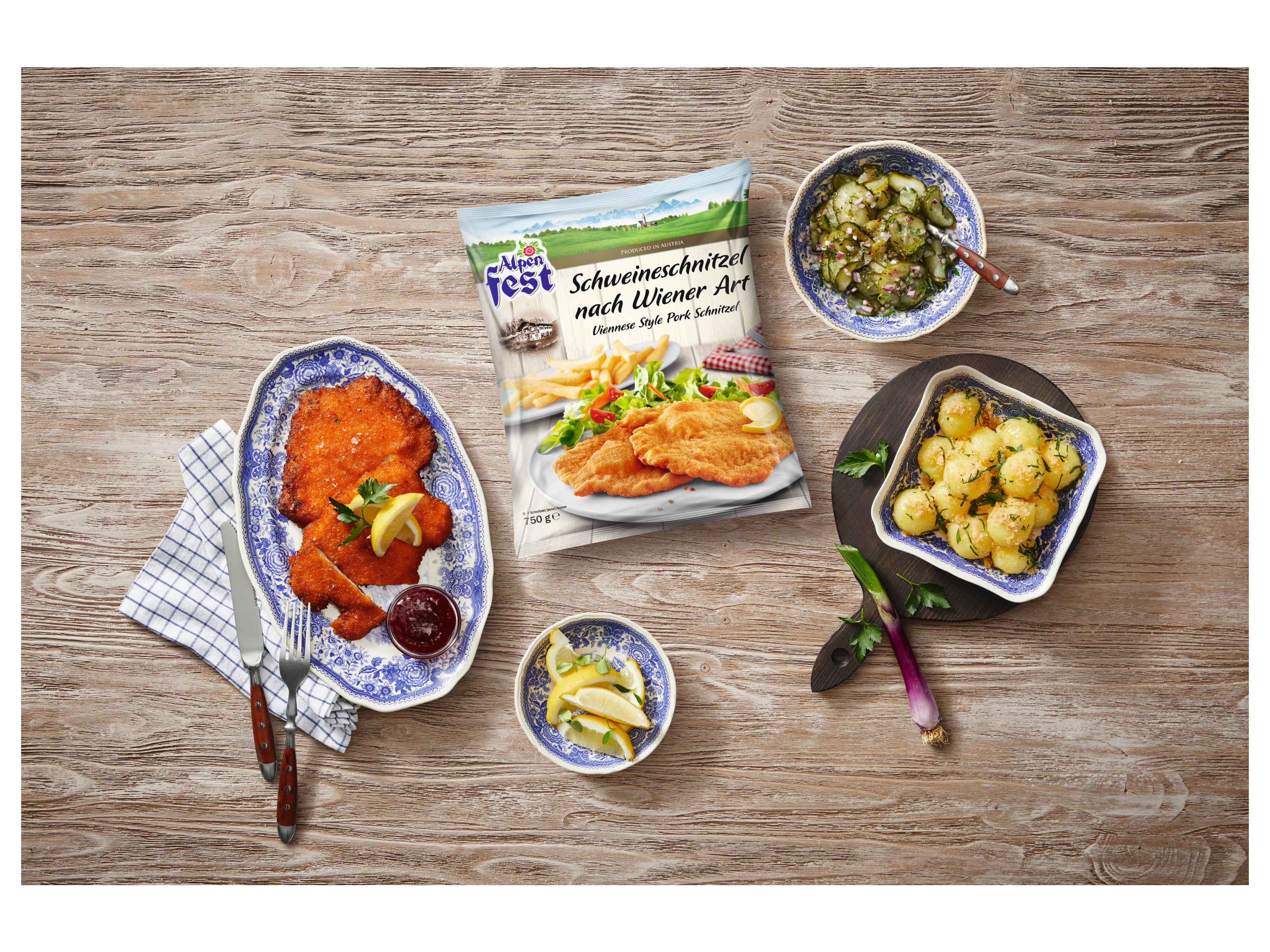 A meal featuring pork schnitzel, potatoes, and cucumber salad, with a package of Alpen Fest schnitzel.