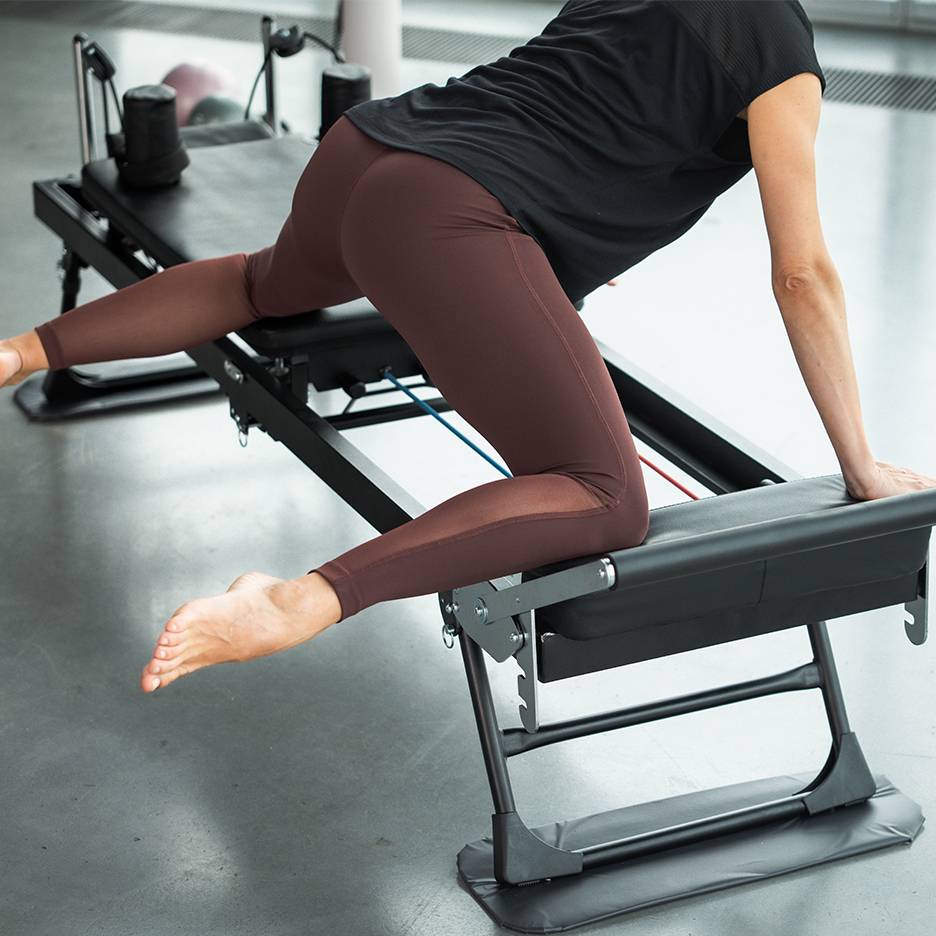 Woman exercising on a Pilates machine, focusing on legs and glutes.