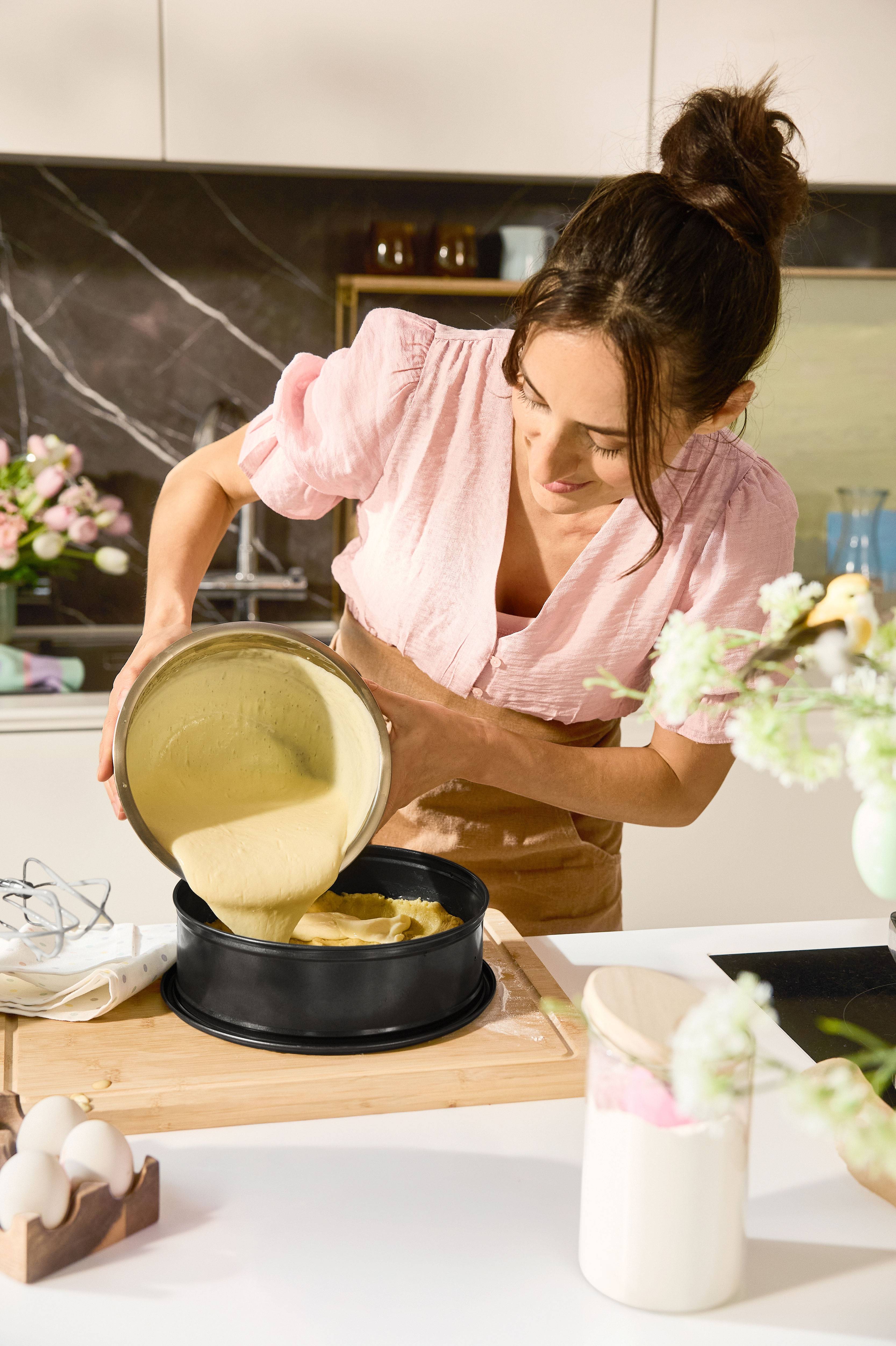 Woman pouring cake batter into a baking pan in the kitchen.