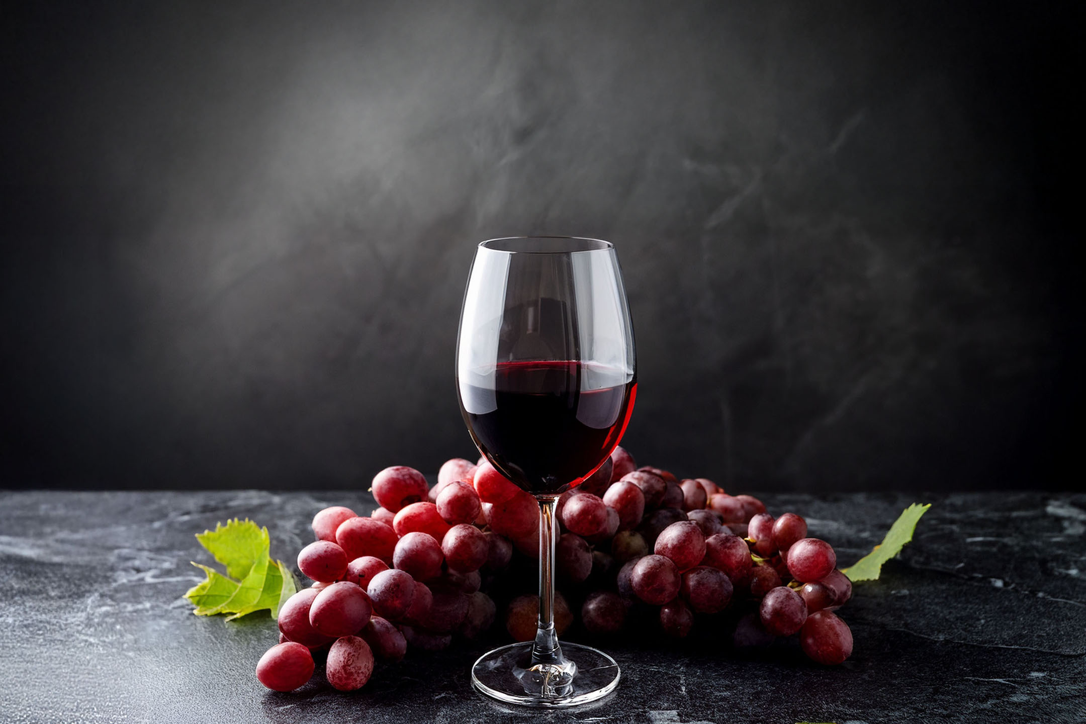 A glass of red wine and a bunch of red grapes on a dark background.