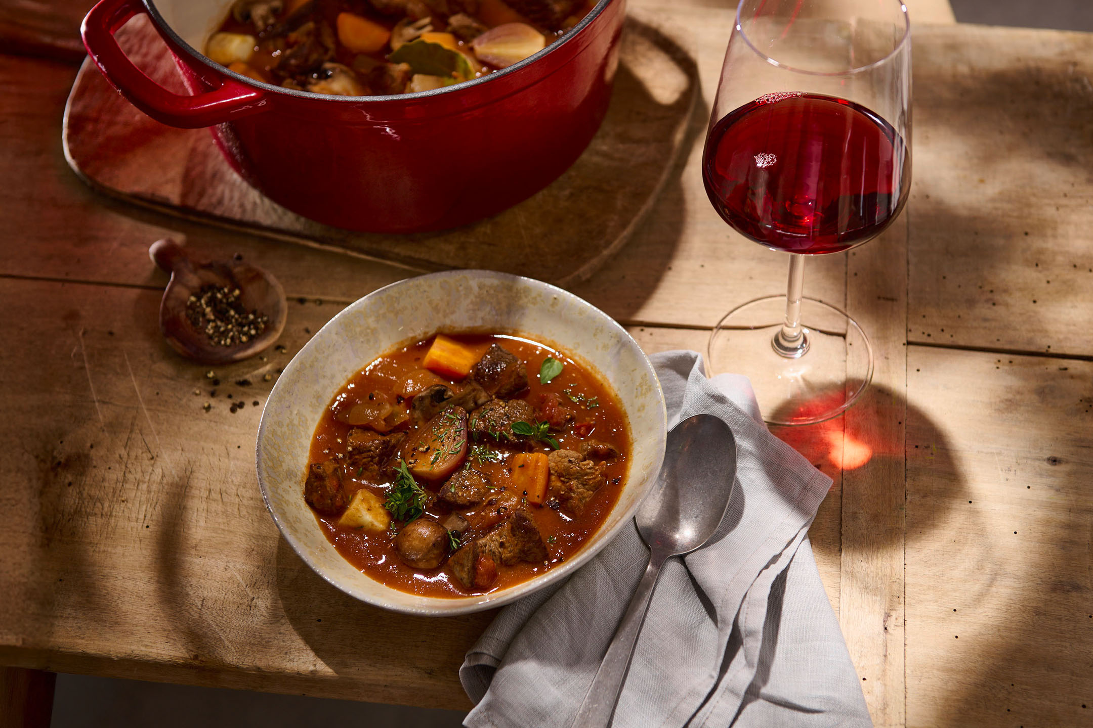 Beef and vegetable stew in a pot and bowl, with a glass of red wine.