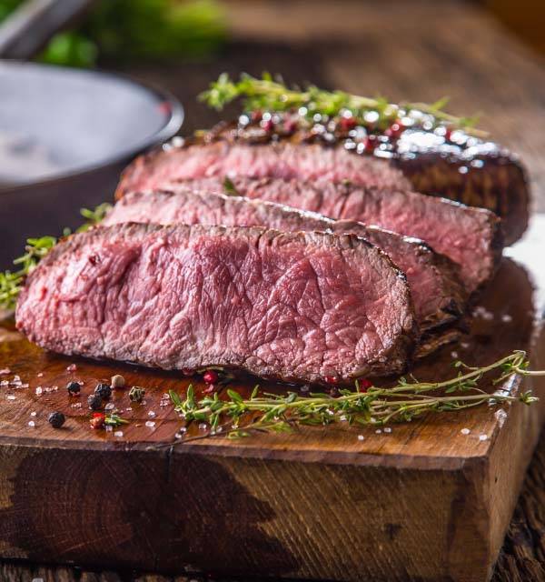 Sliced steak with herbs and spices on a wooden cutting board.