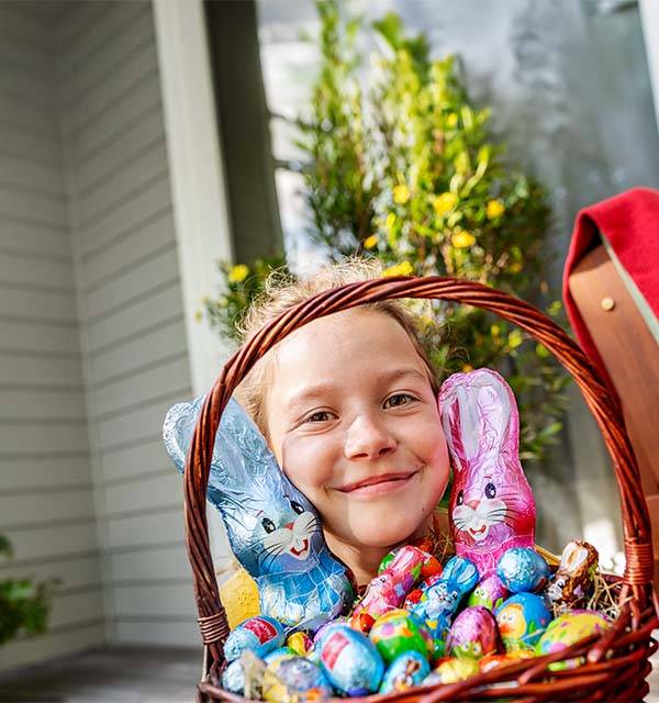 Smiling child with a basket of chocolate Easter bunnies and eggs.