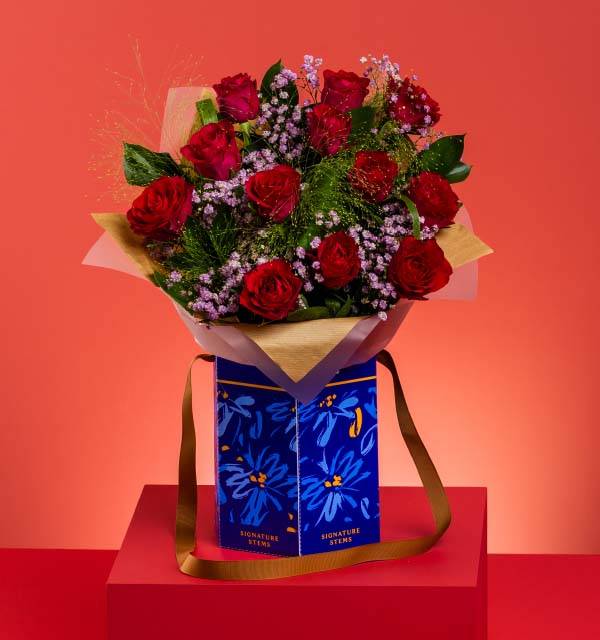 Red roses and purple flowers in a blue gift box with a gold ribbon on a red background.