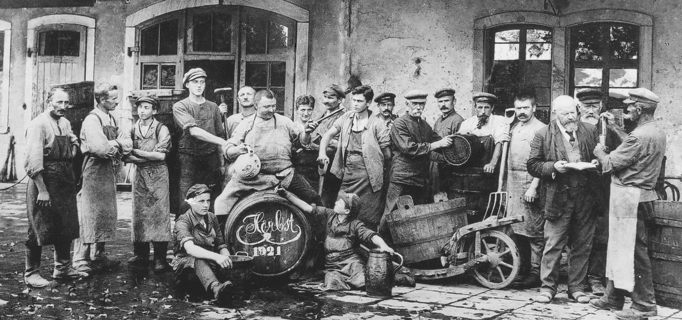 Men in a cellar with wine barrels, one raising a glass.