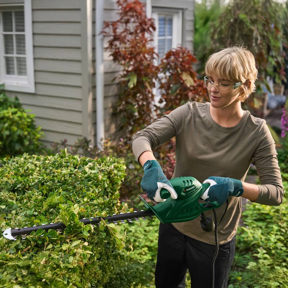 Woman trimming a hedge with green Parkside hedge shears.