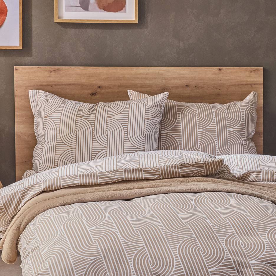 Bedding set with brown and white geometric pattern, a soft blanket on a bed with a wooden headboard.