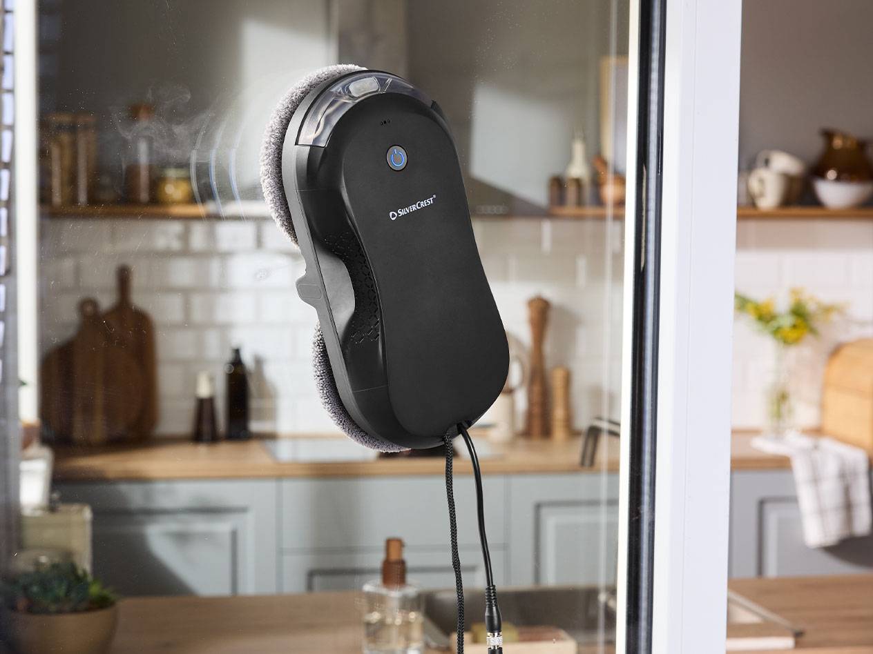 Silvercrest window cleaning robot on a window pane with a kitchen in the background.