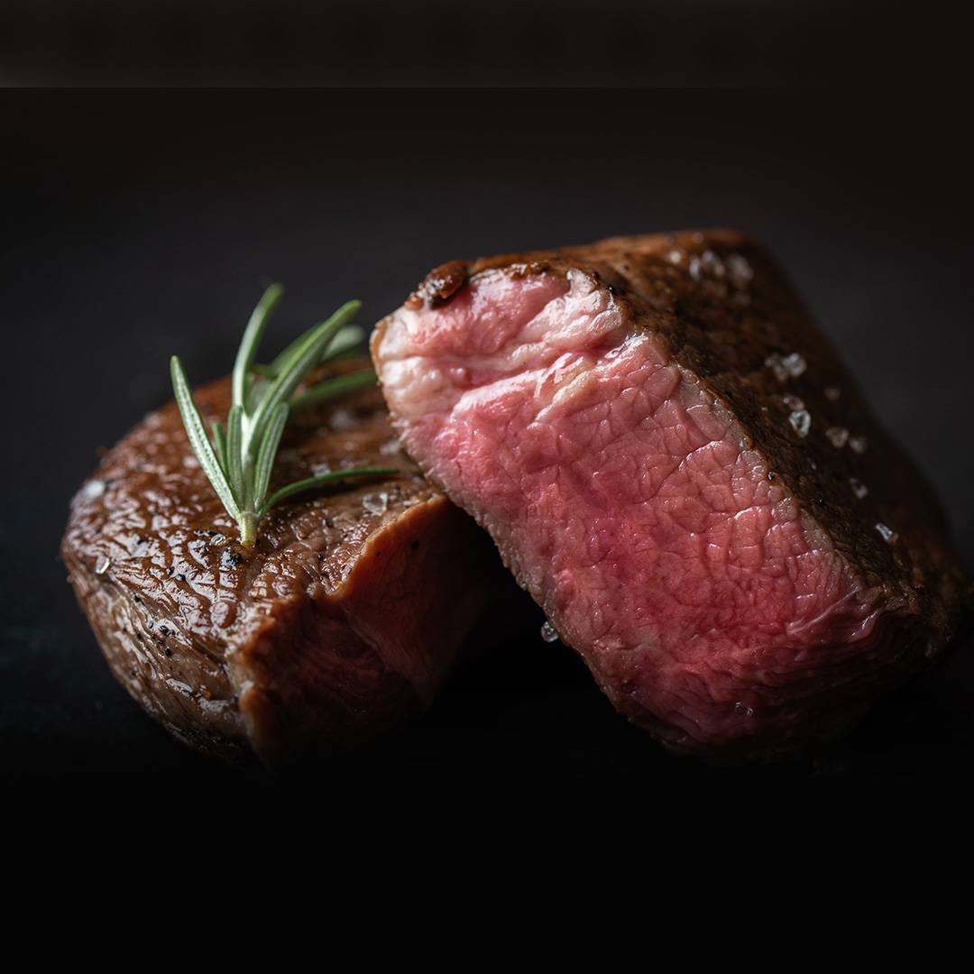 Perfectly cooked steak, medium-rare, with rosemary and sea salt on a dark background.