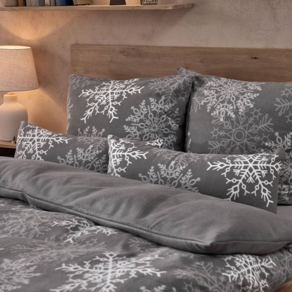 Gray bedding with white snowflakes, featuring pillows and a fluffy blanket.
