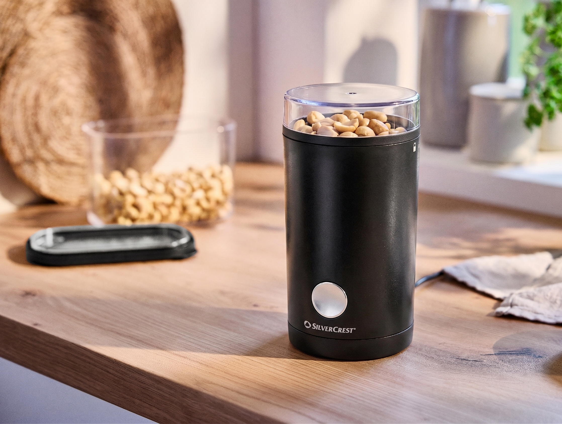 Black nut grinder with peanuts on a wooden kitchen countertop.