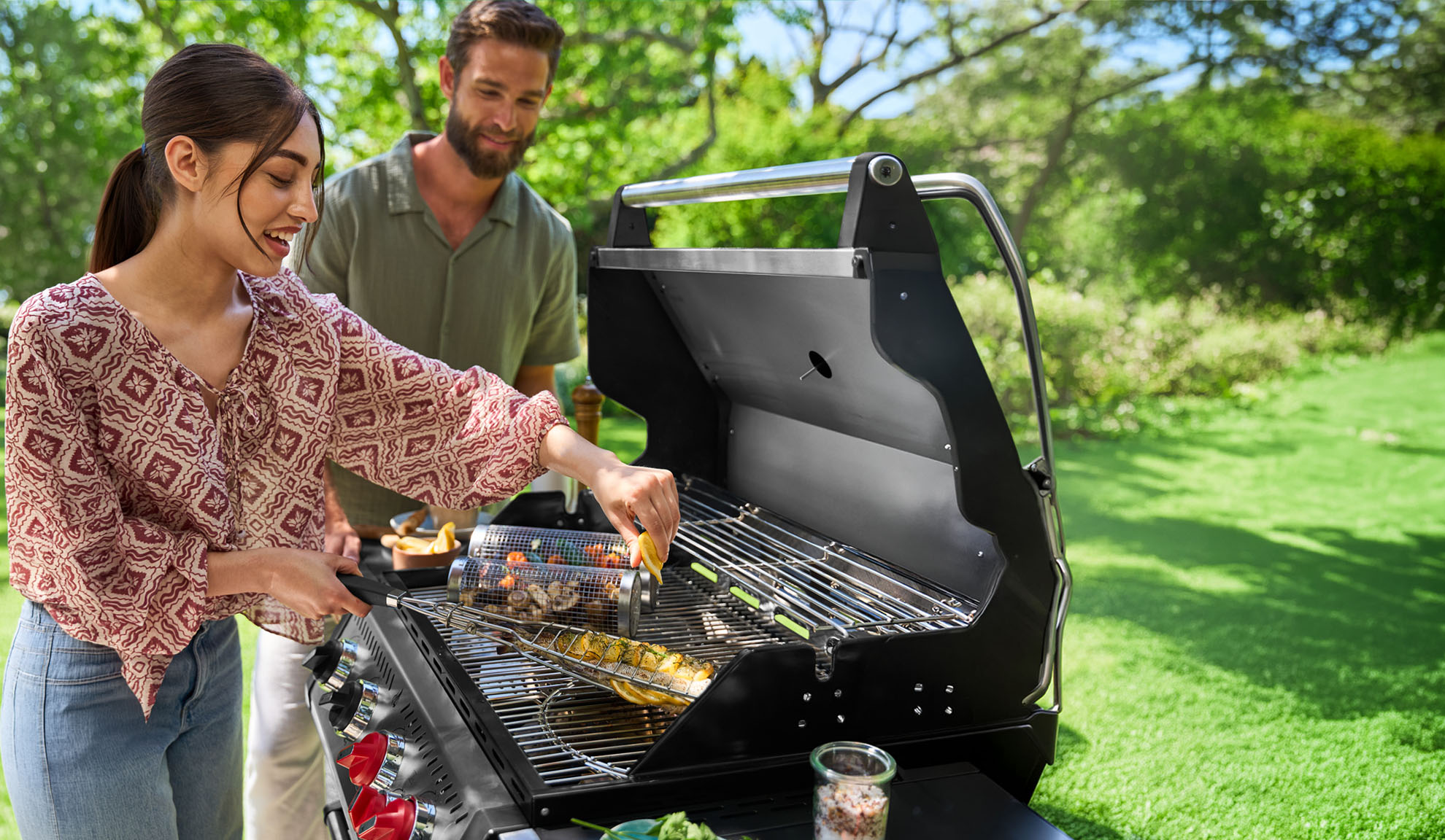 Couple barbecuing outdoors, woman squeezing lemon onto fish.