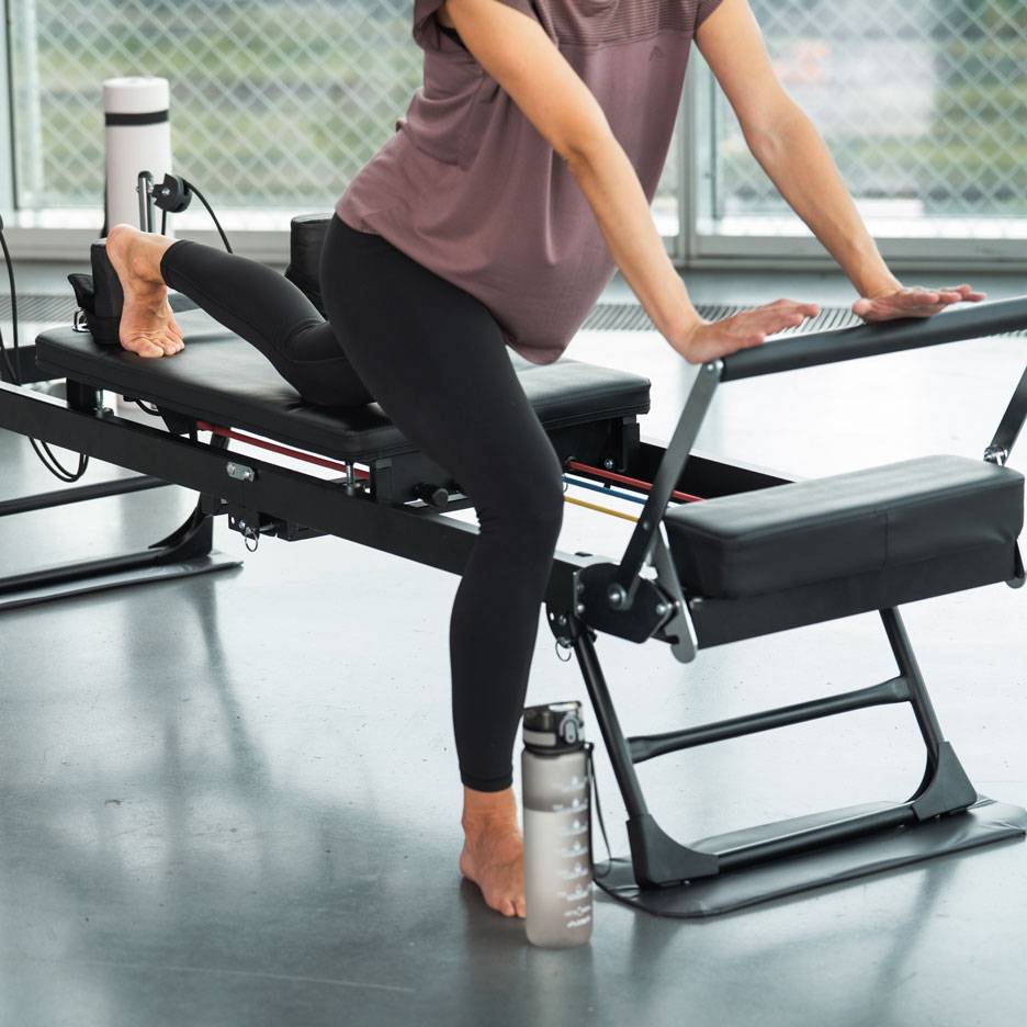 Woman exercising on a Pilates machine with a water bottle nearby.