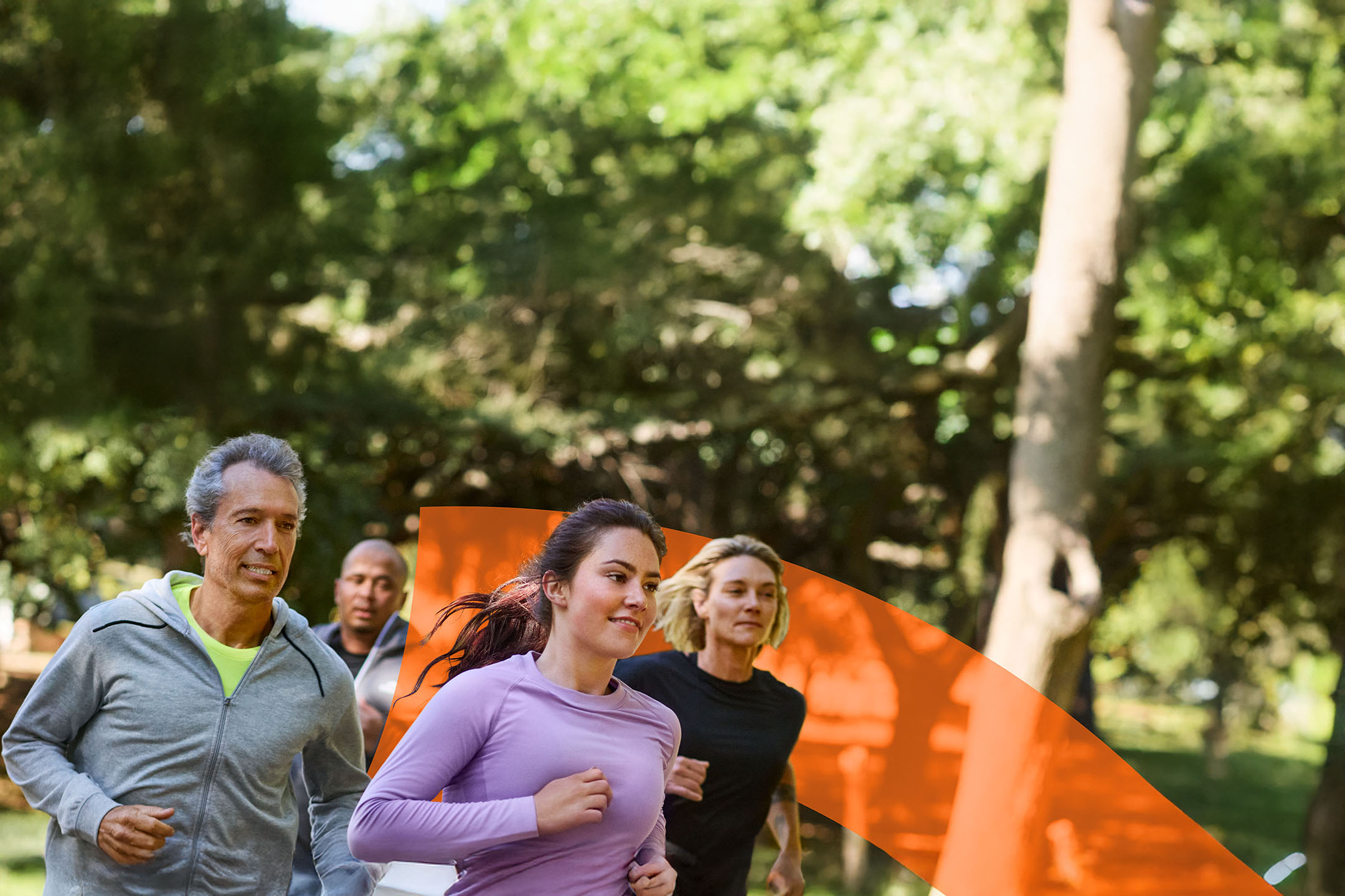Four runners in athletic wear are jogging outdoors in a park.