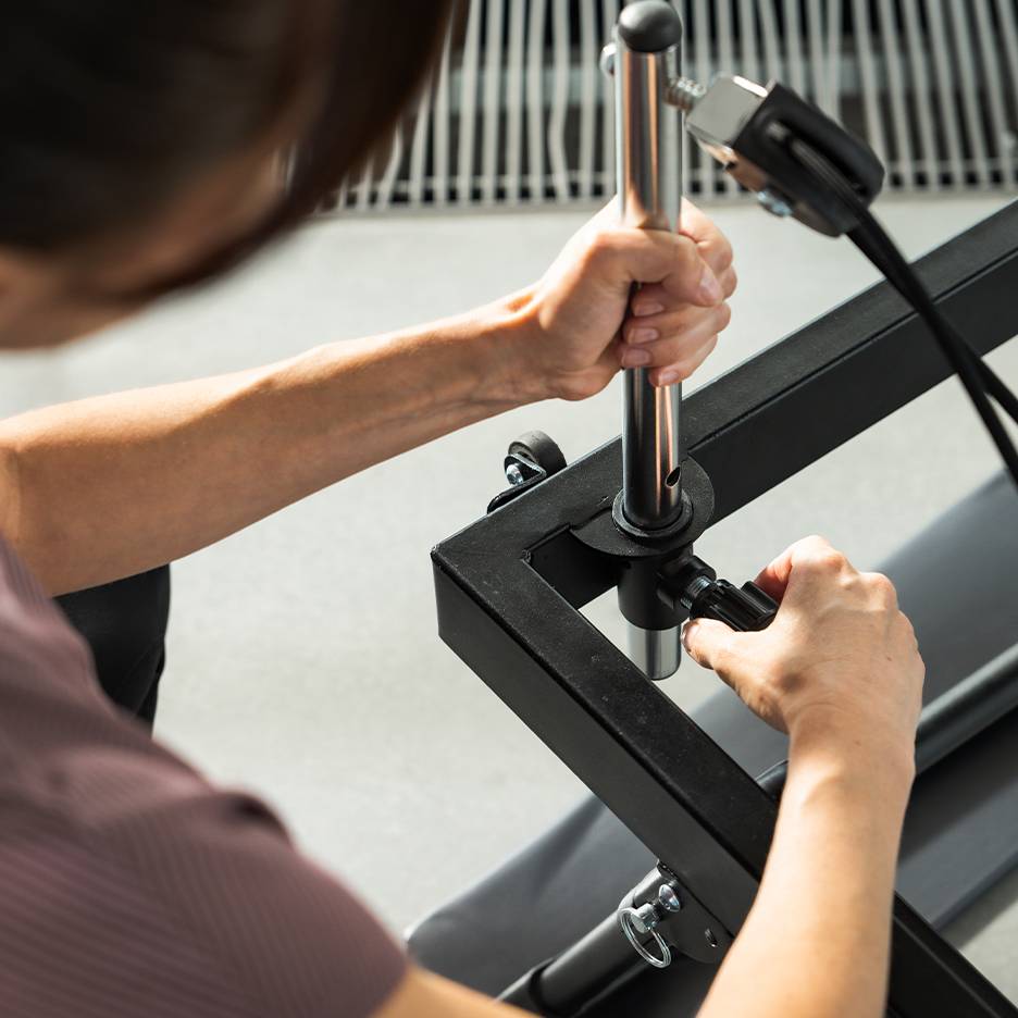 Person adjusting a piece of fitness equipment, focusing on the hands and metal parts.