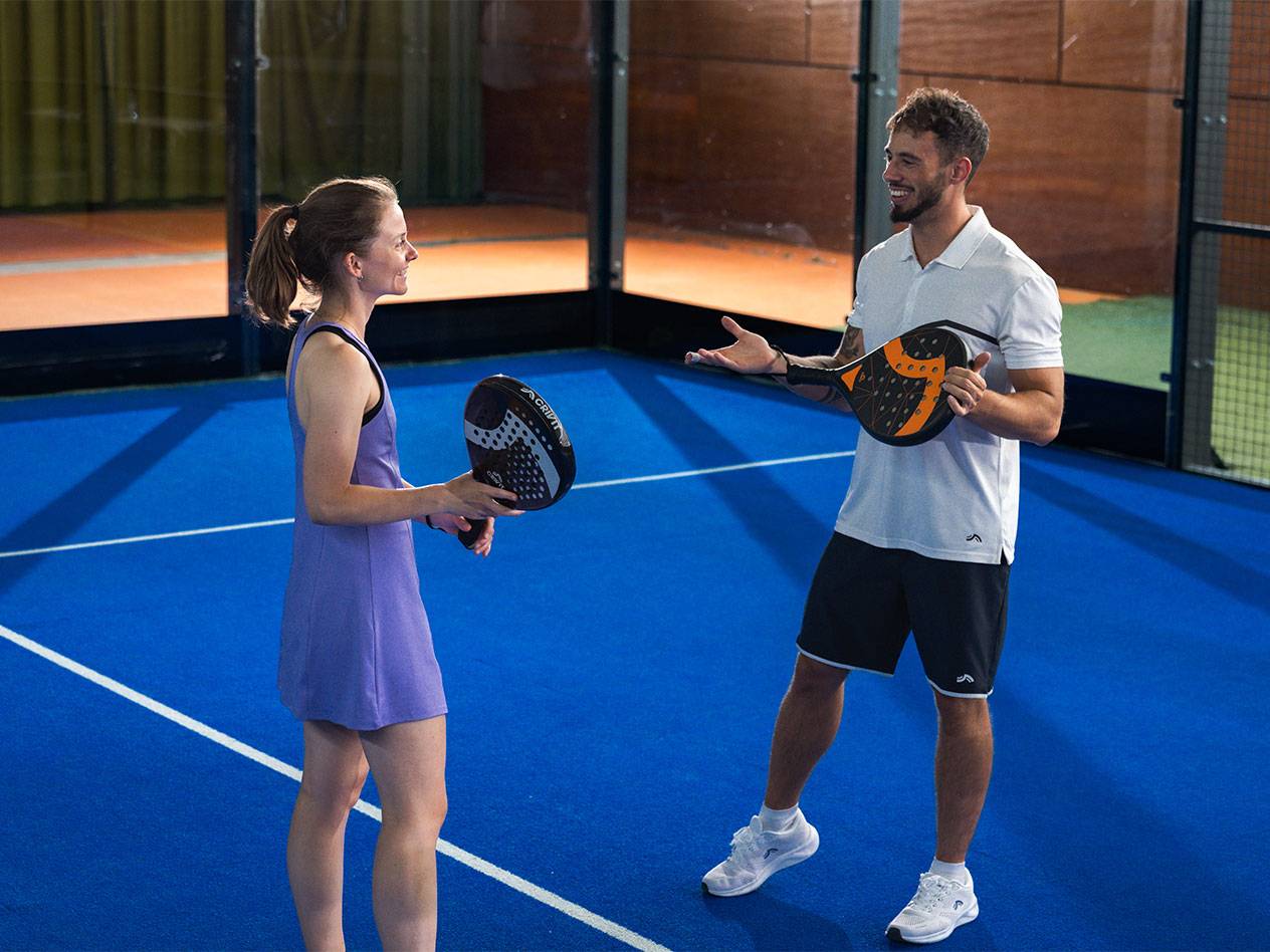 Man and woman with padel rackets on blue court, ready to play.