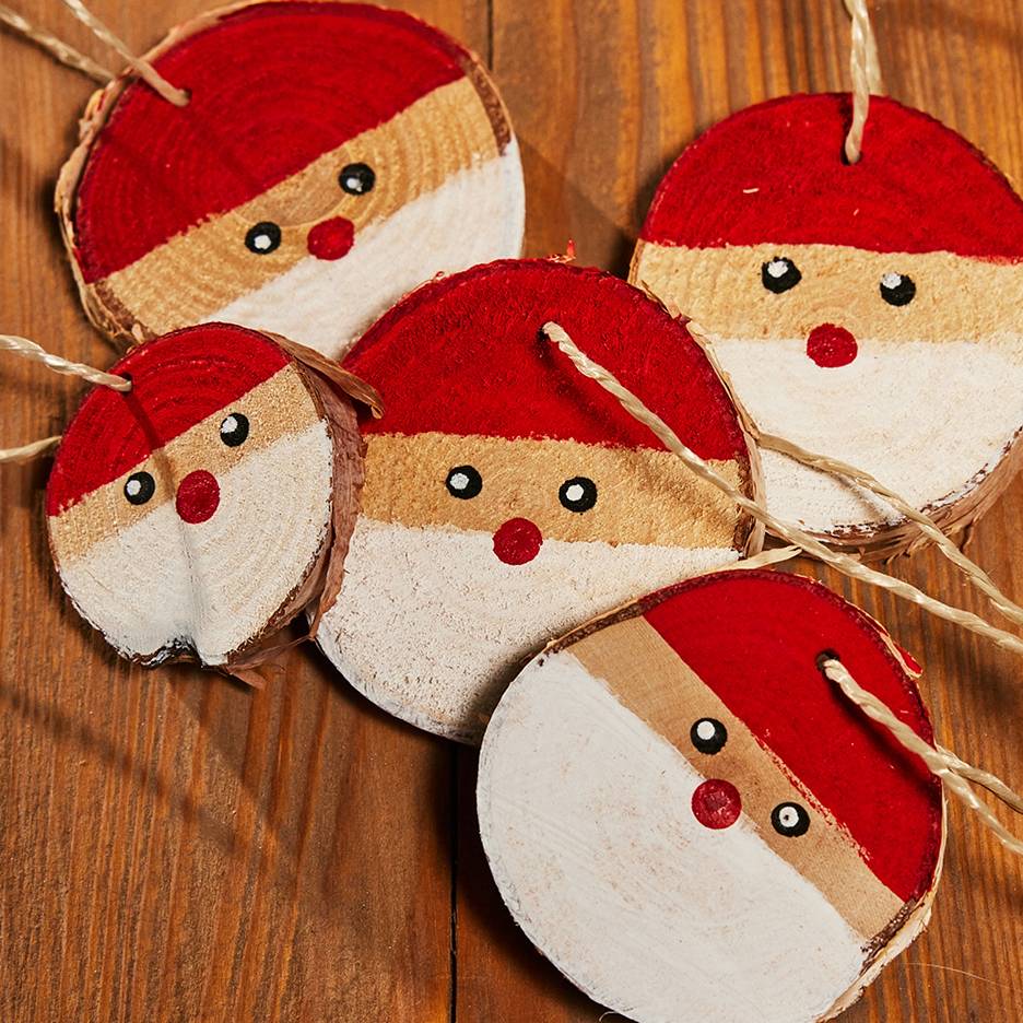 Five hand-painted Santa Claus ornaments made from wood slices with strings, lying on a wooden table.