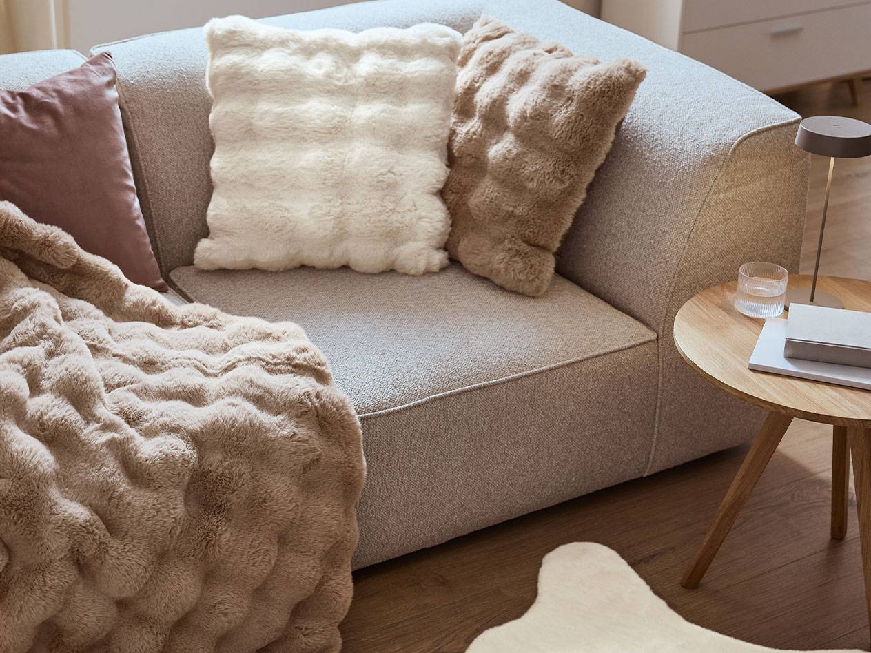 Sofa with fluffy pillows and blanket, next to a wooden side table with a lamp.
